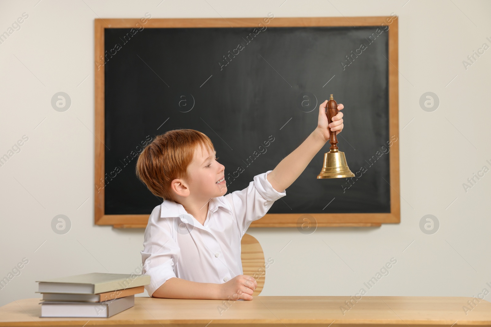 Photo of Cute little boy ringing school bell in classroom