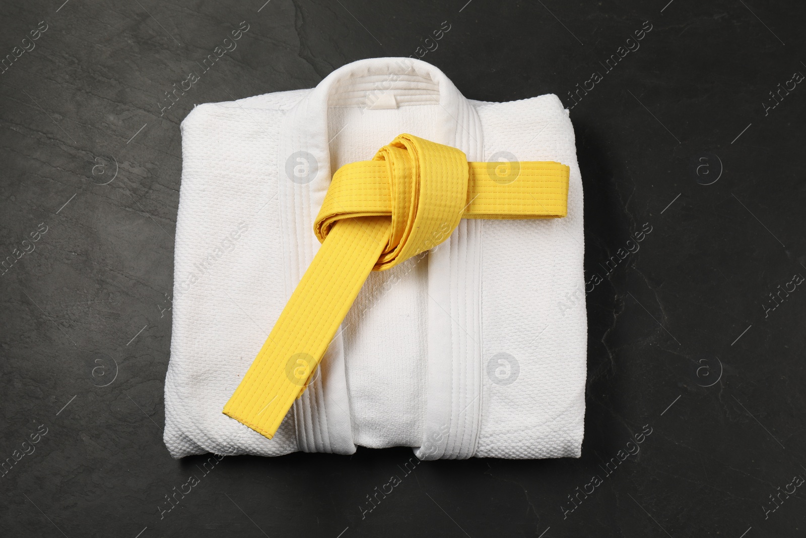 Photo of Yellow karate belt and white kimono on gray background, top view