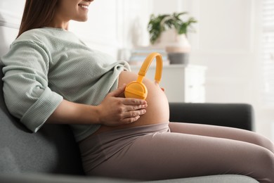Photo of Pregnant woman with headphones on her belly at home, closeup