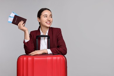 Happy businesswoman with passport, tickets and suitcase on grey background. Space for text