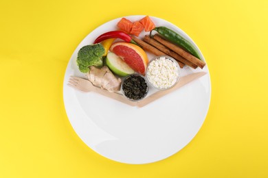 Photo of Metabolism. Plate with different food products and wooden cutlery on yellow background, top view