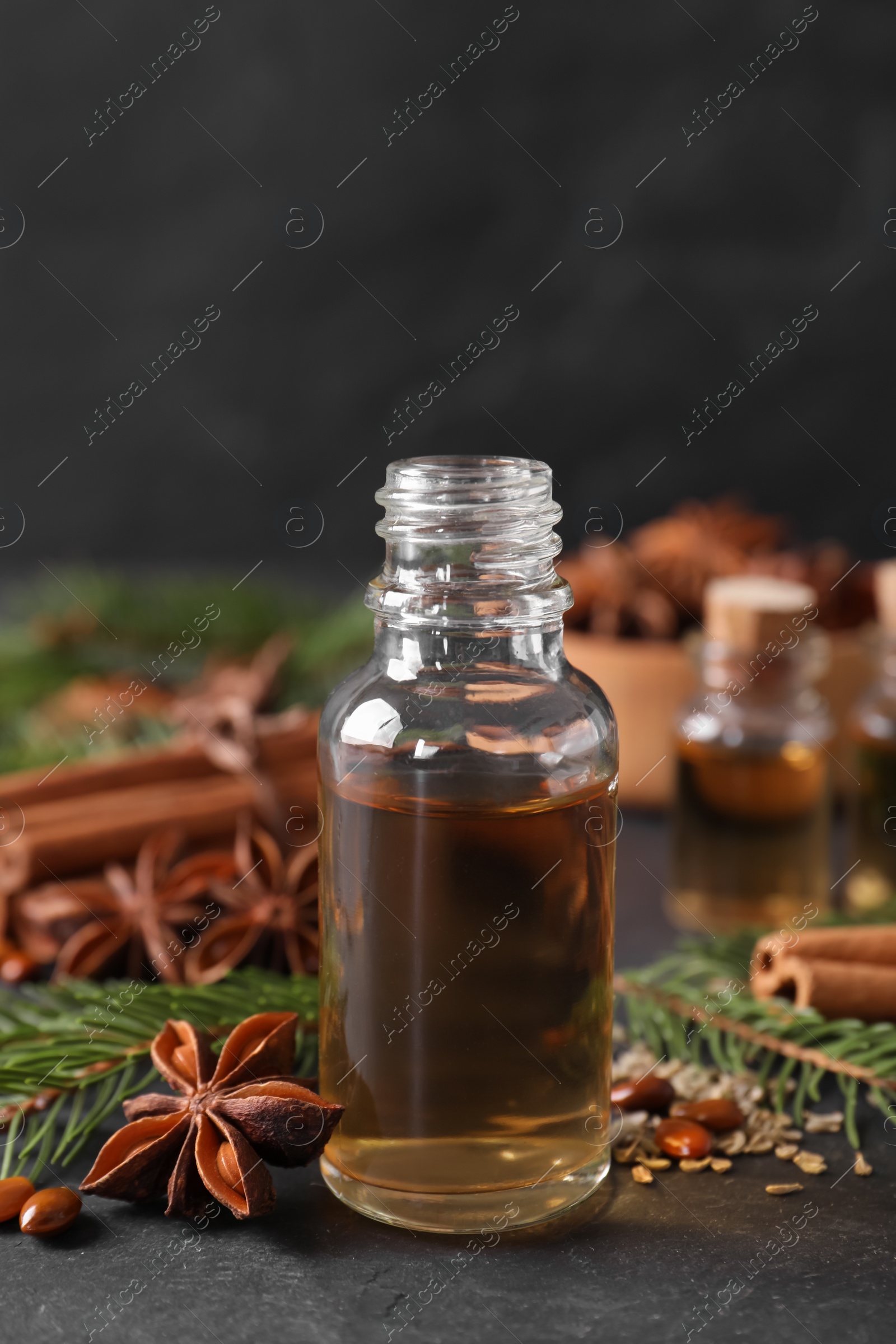 Photo of Bottle of essential oil, anise, cinnamon and fir tree branches on black table