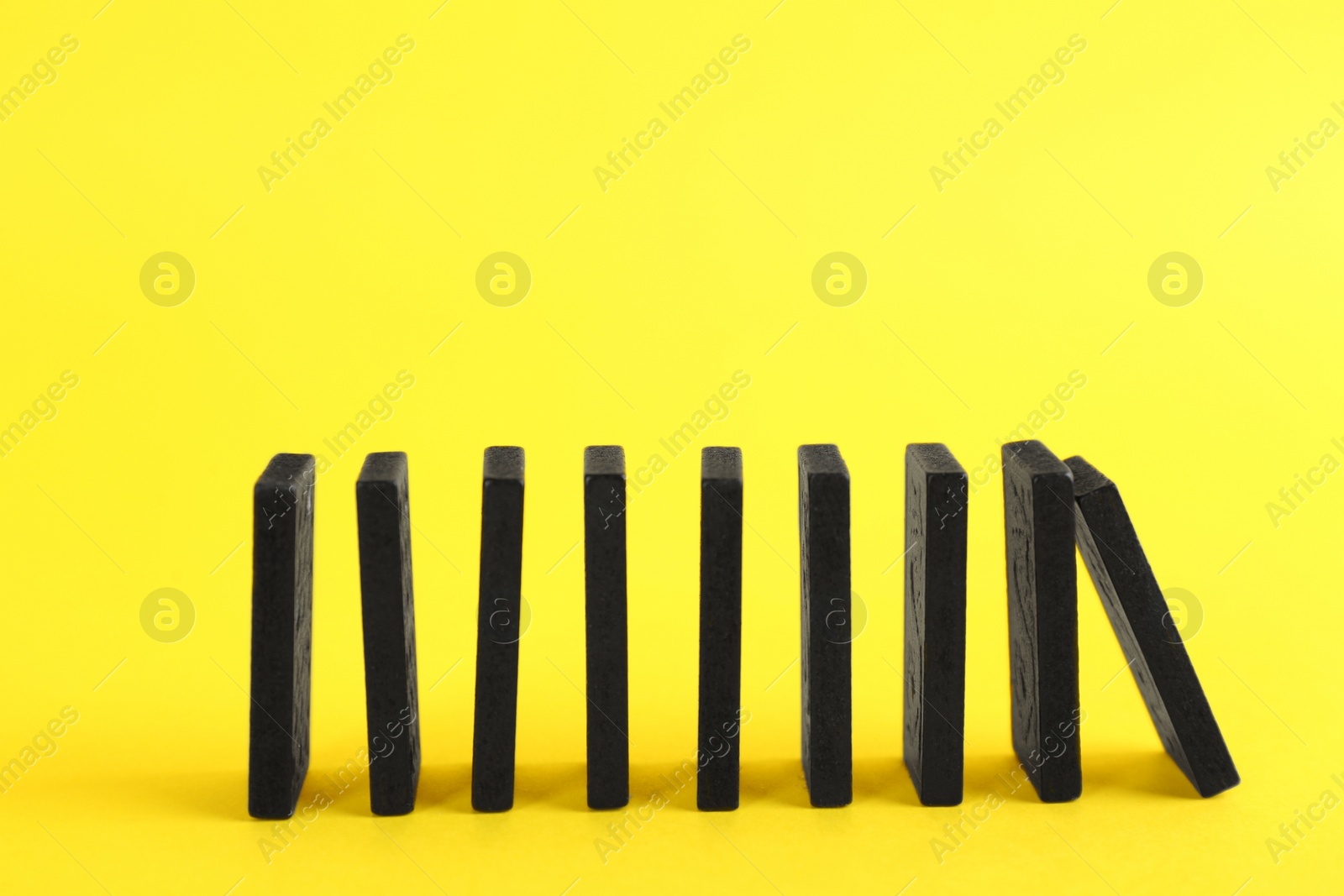 Photo of Black domino tiles falling on yellow background. Space for text