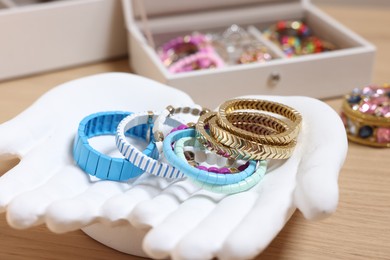 Photo of Ceramic hand stand with many different bracelets on wooden table, closeup