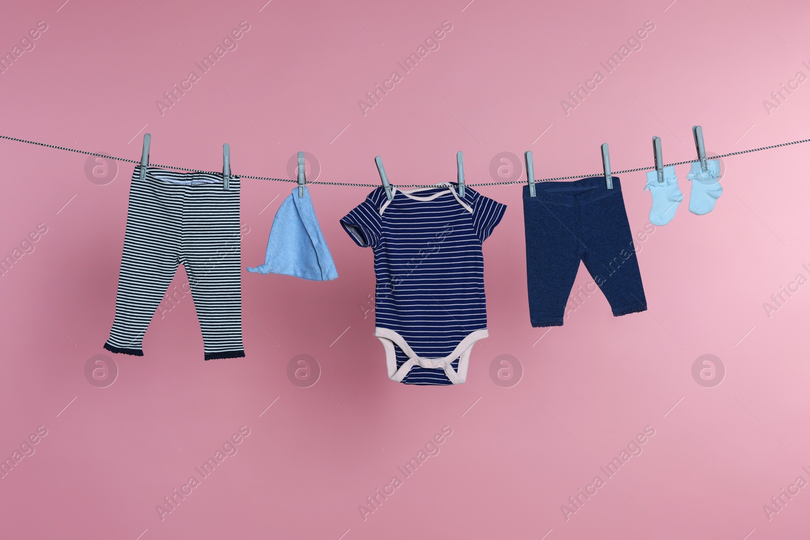 Photo of Different baby clothes drying on laundry line against pink background