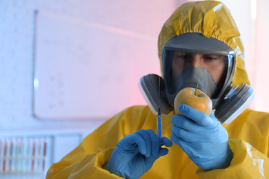 Photo of Scientist in chemical protective suit with apple and syringe at laboratory, space for text