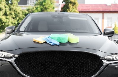 Photo of Sponges and rags on car hood outdoors. Cleaning products