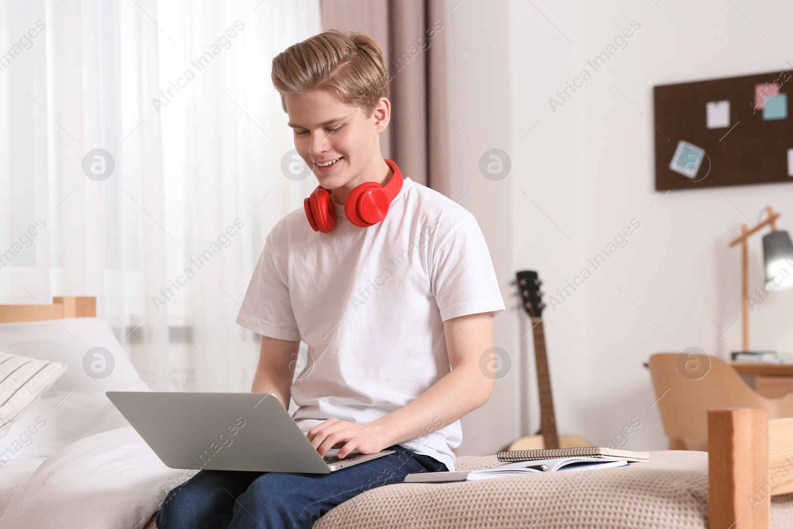 Photo of Online learning. Smiling teenage boy typing on laptop at home