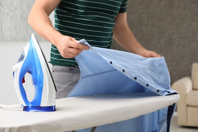 Man ironing shirt on board at home, closeup