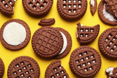 Photo of Tasty chocolate sandwich cookies with cream on yellow background, flat lay