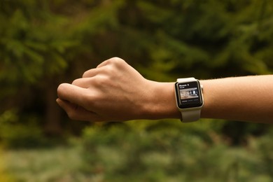 Woman checking home security system via smartwatch app outdoors, closeup. Image of room through CCTV camera on display