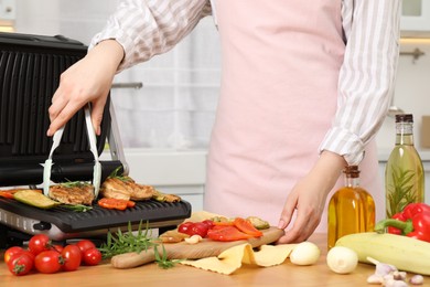 Photo of Woman cooking different products with electric grill at wooden table in kitchen, closeup