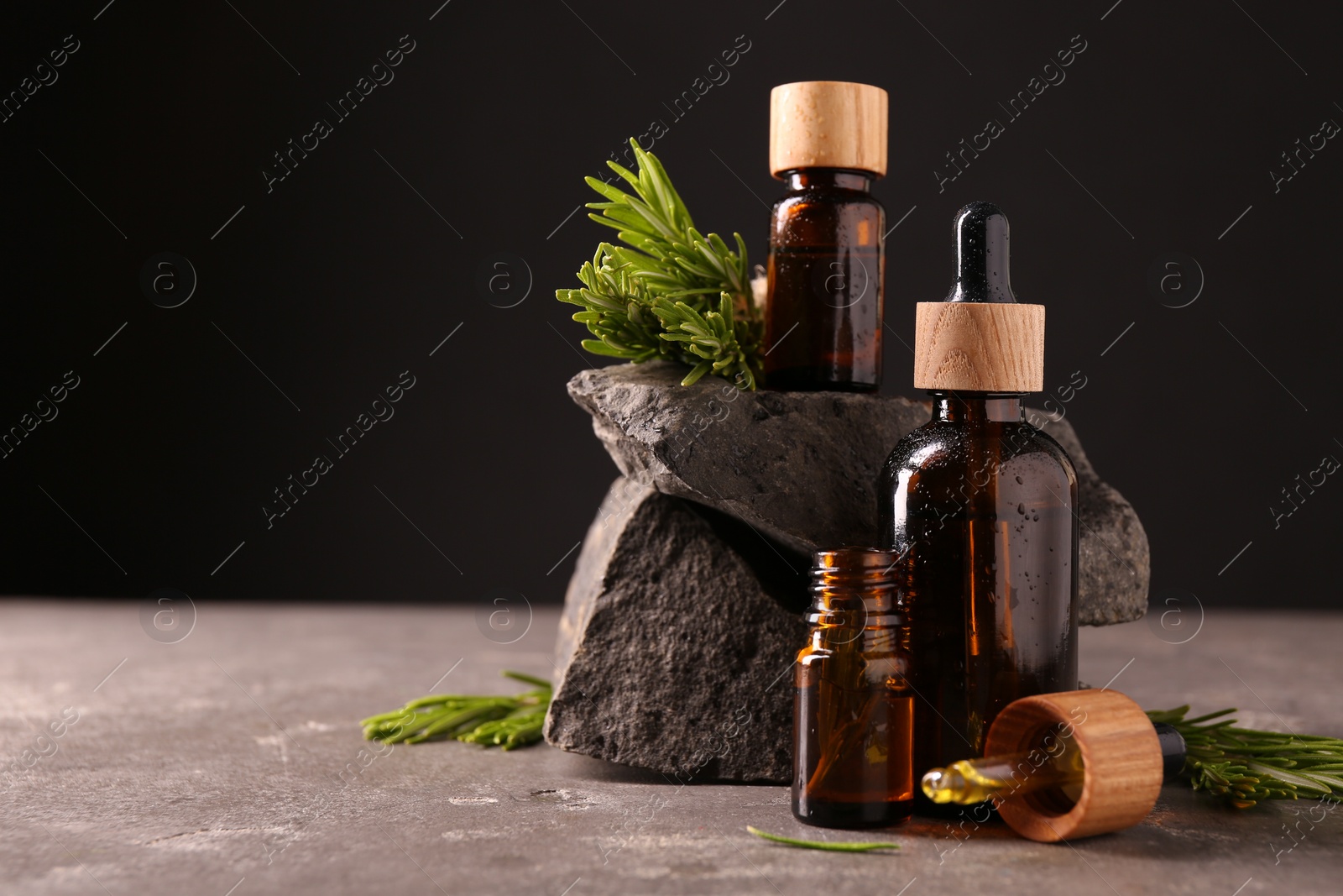 Photo of Essential oil in bottles, dropper and rosemary on grey table, space for text