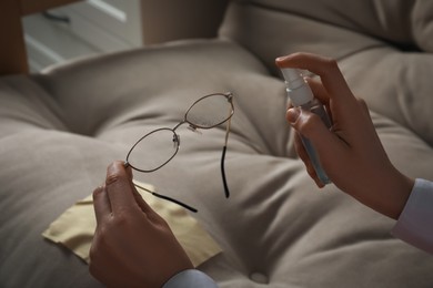 Woman cleaning glasses with spray indoors, closeup