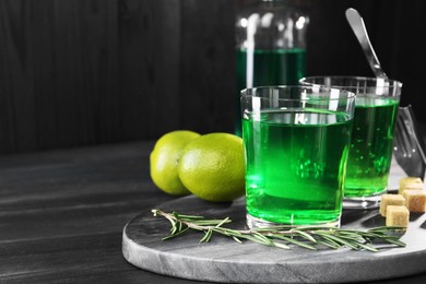 Photo of Absinthe in glasses, rosemary, brown sugar and lime on black wooden table, space for text. Alcoholic drink