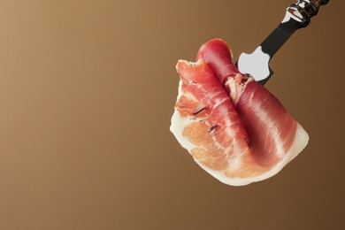 Photo of Fork with slice of tasty jamon on brown background, closeup. Space for text