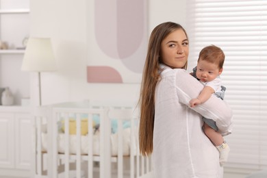 Mother holding her cute newborn baby in child's room, space for text