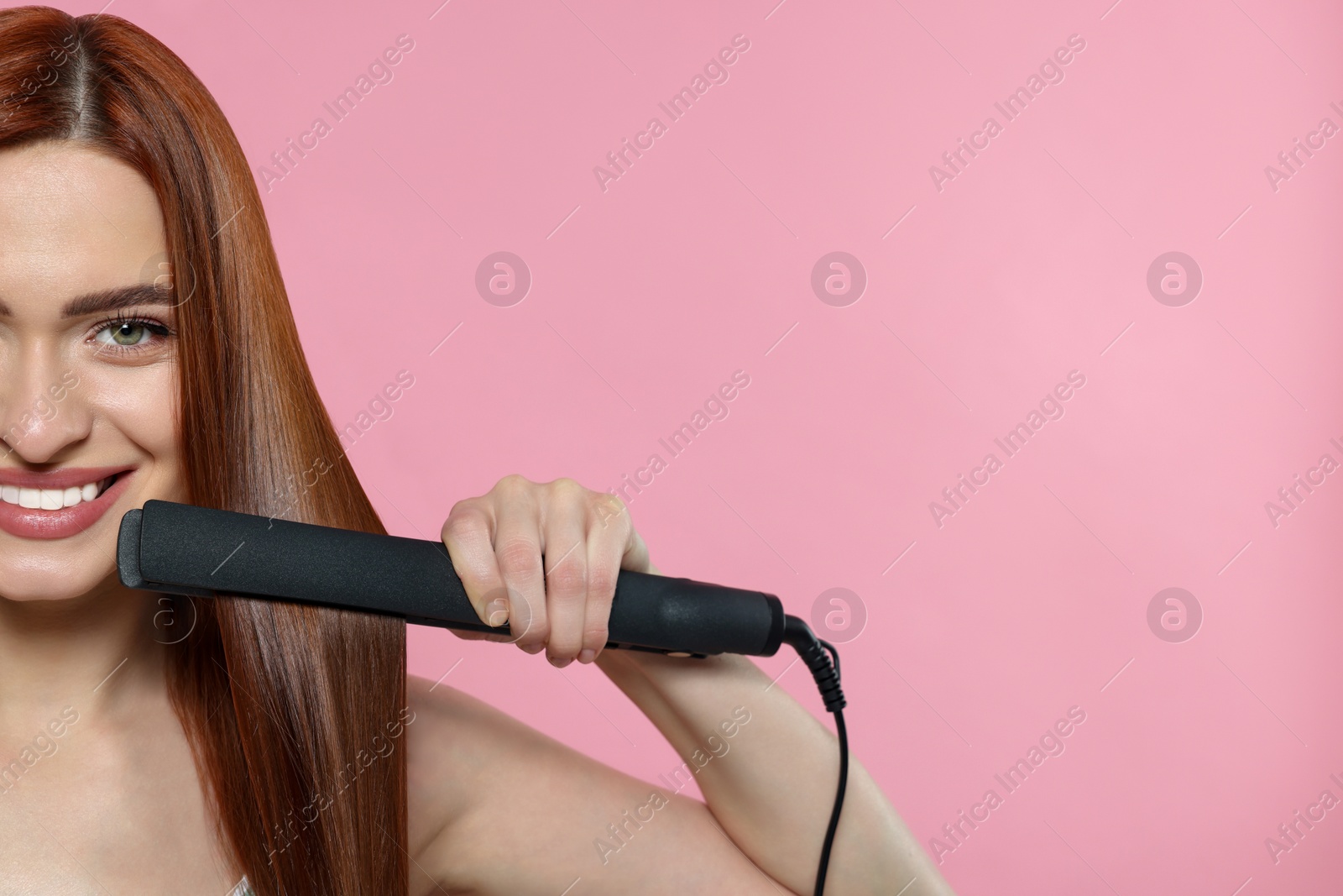 Photo of Beautiful woman using hair iron on pink background, closeup. Space for text