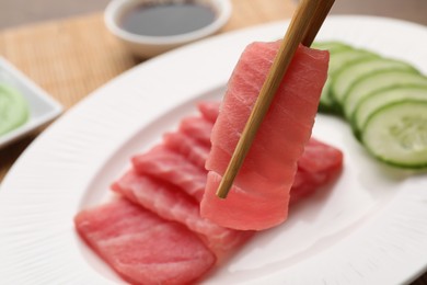 Holding tasty sashimi (piece of fresh raw tuna) with chopsticks against blurred background, closeup