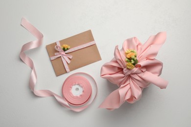 Photo of Furoshiki technique. Gift packed in pink fabric, card, flowers and ribbon on white table, flat lay