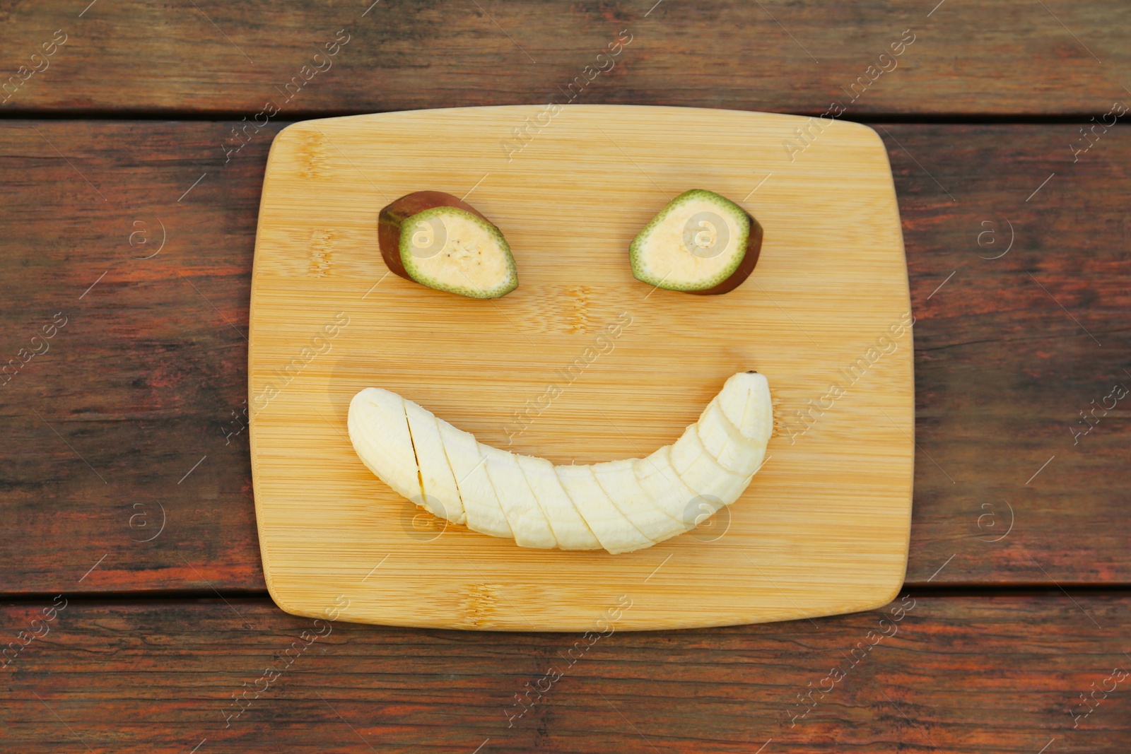 Photo of Smiley face made with banana slices on wooden table, top view