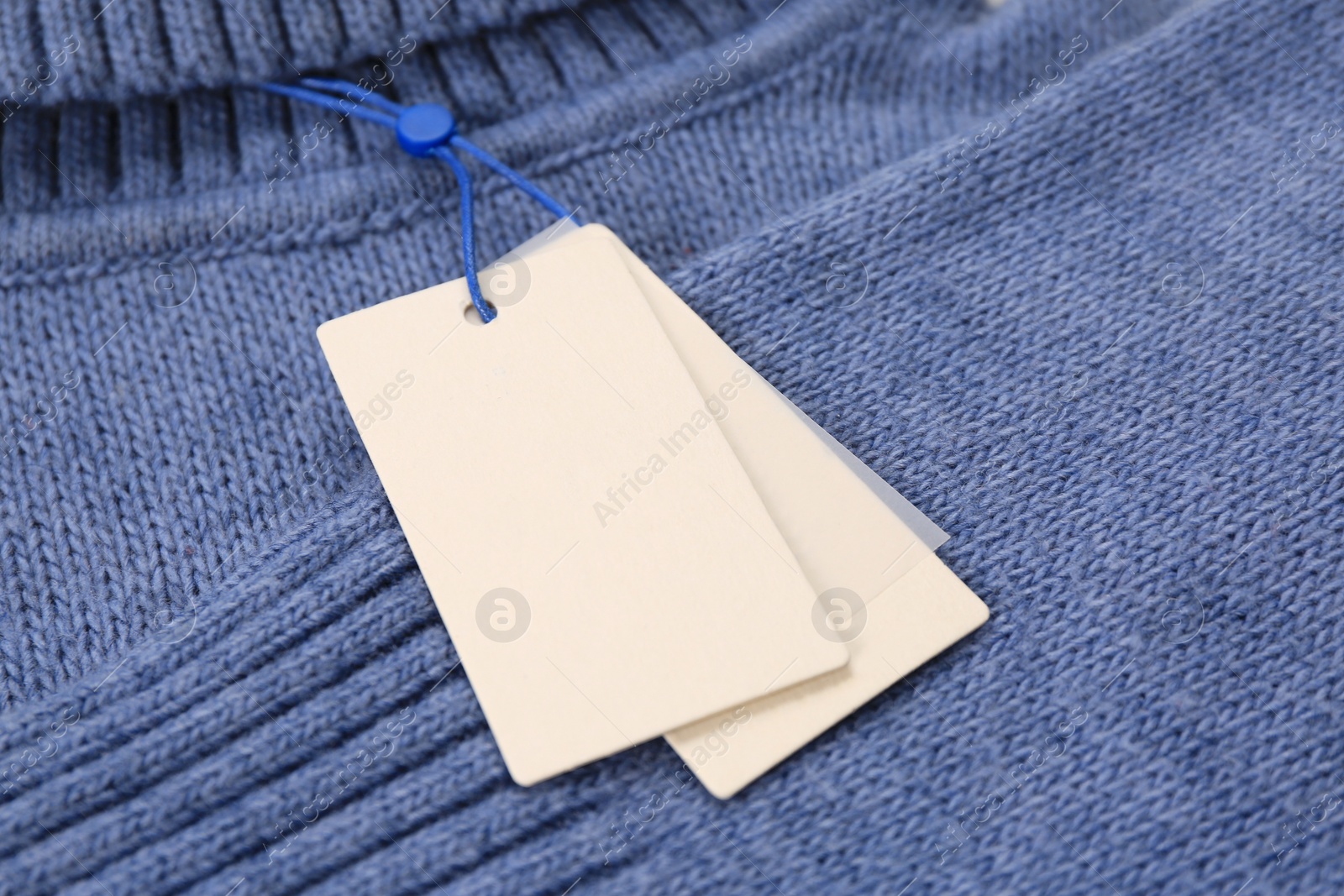 Photo of Blank white tags on blue knitted sweater, closeup. Space for text