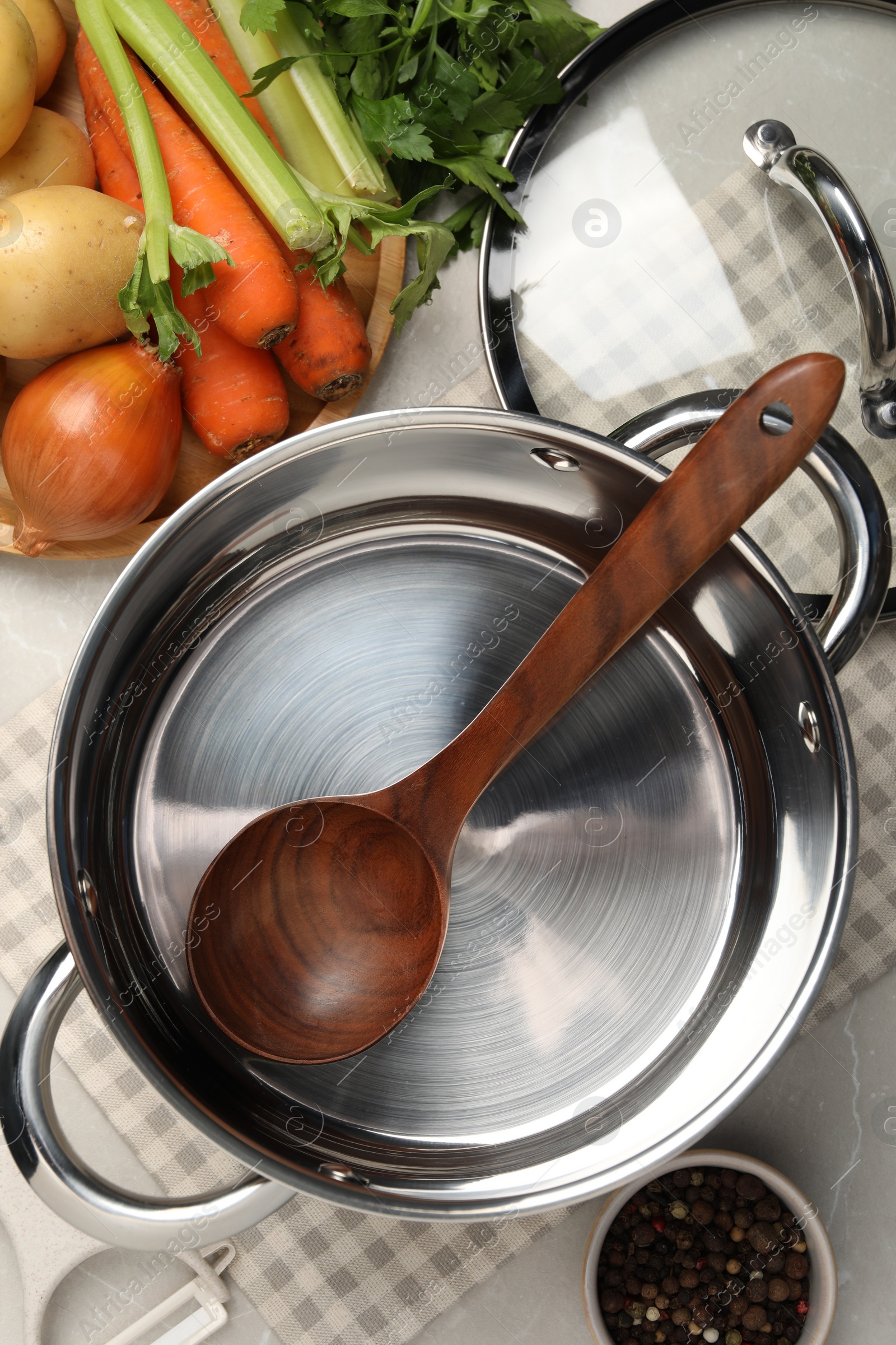 Photo of Pot with ladle and different ingredients for cooking tasty bouillon on light table, flat lay