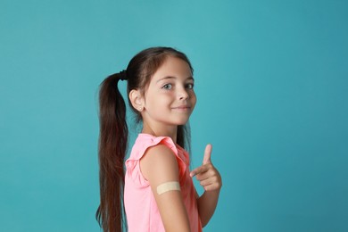 Photo of Vaccinated little girl showing medical plaster on her arm against light blue background