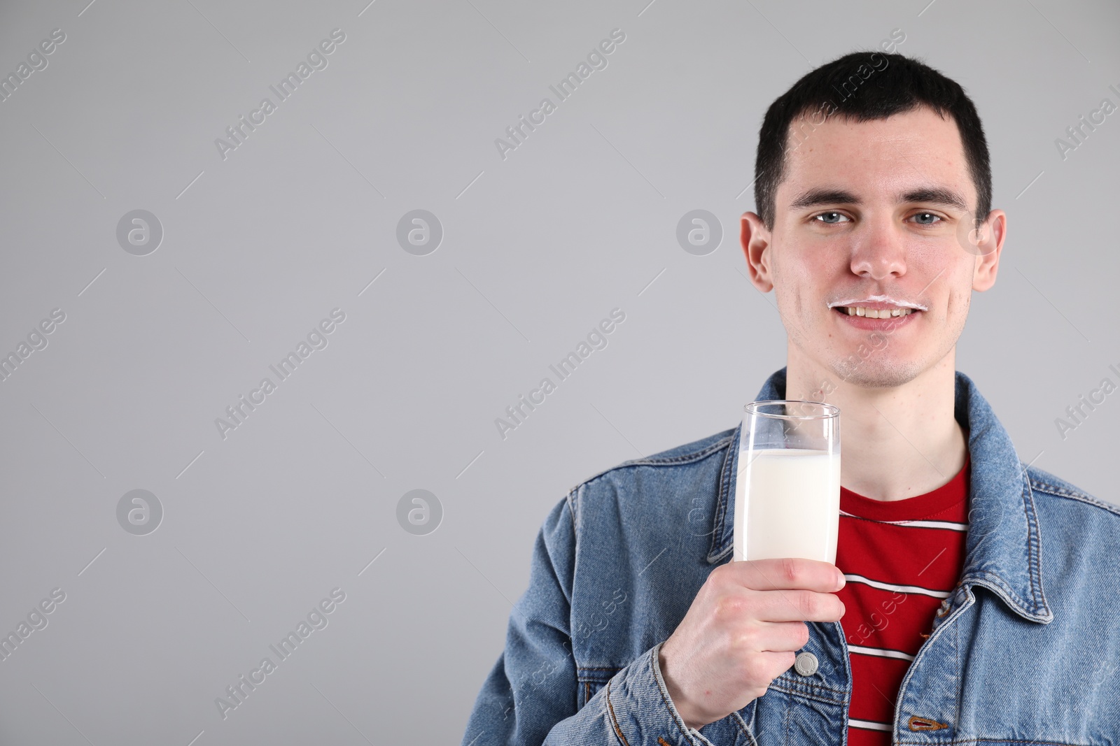 Photo of Happy man with milk mustache holding glass of tasty dairy drink on gray background, space for text