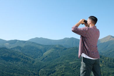 Man looking through binoculars in mountains on sunny day