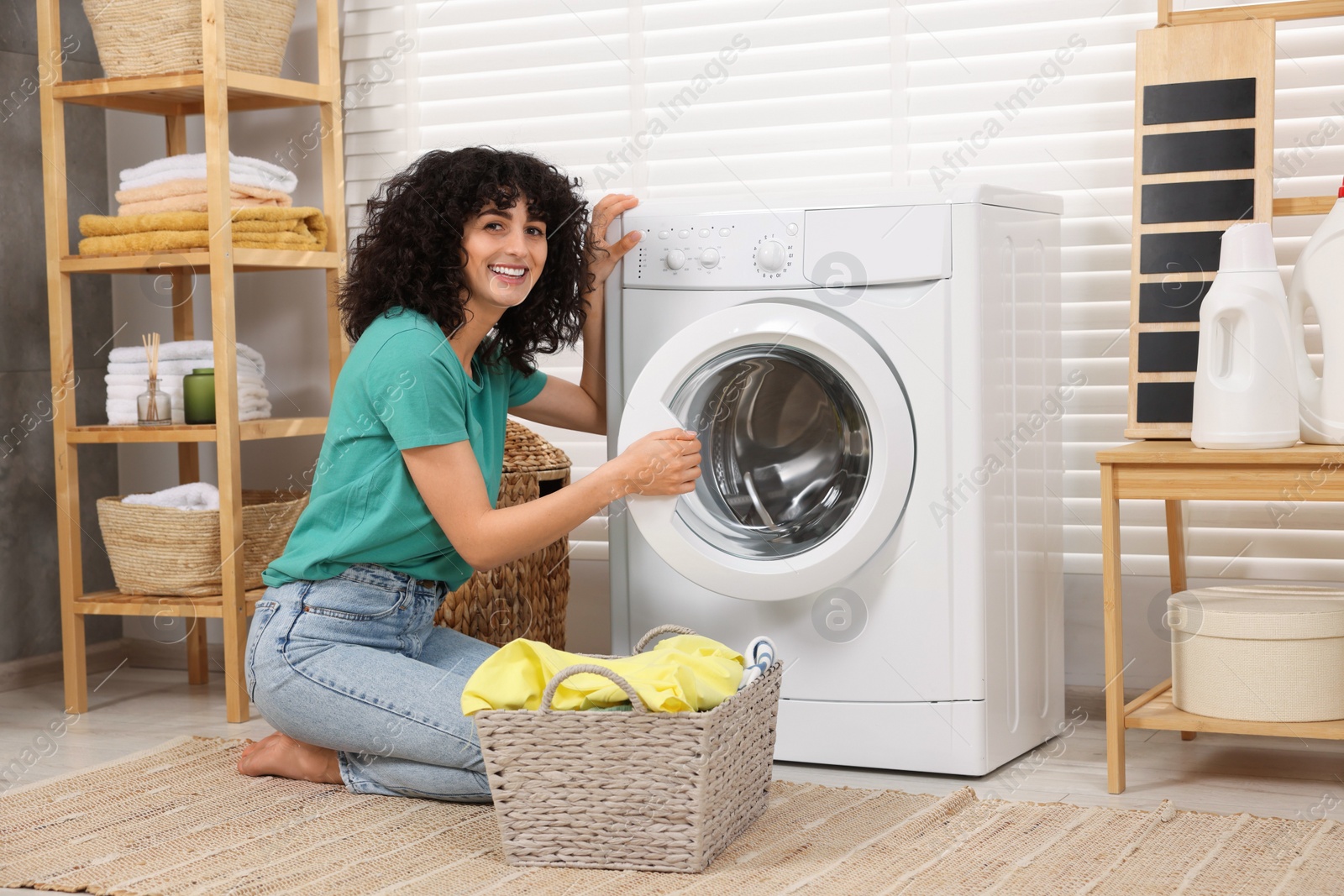 Photo of Happy woman with laundry near washing machine indoors