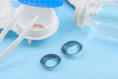 Photo of Case with color contact lenses and tweezers on light blue background