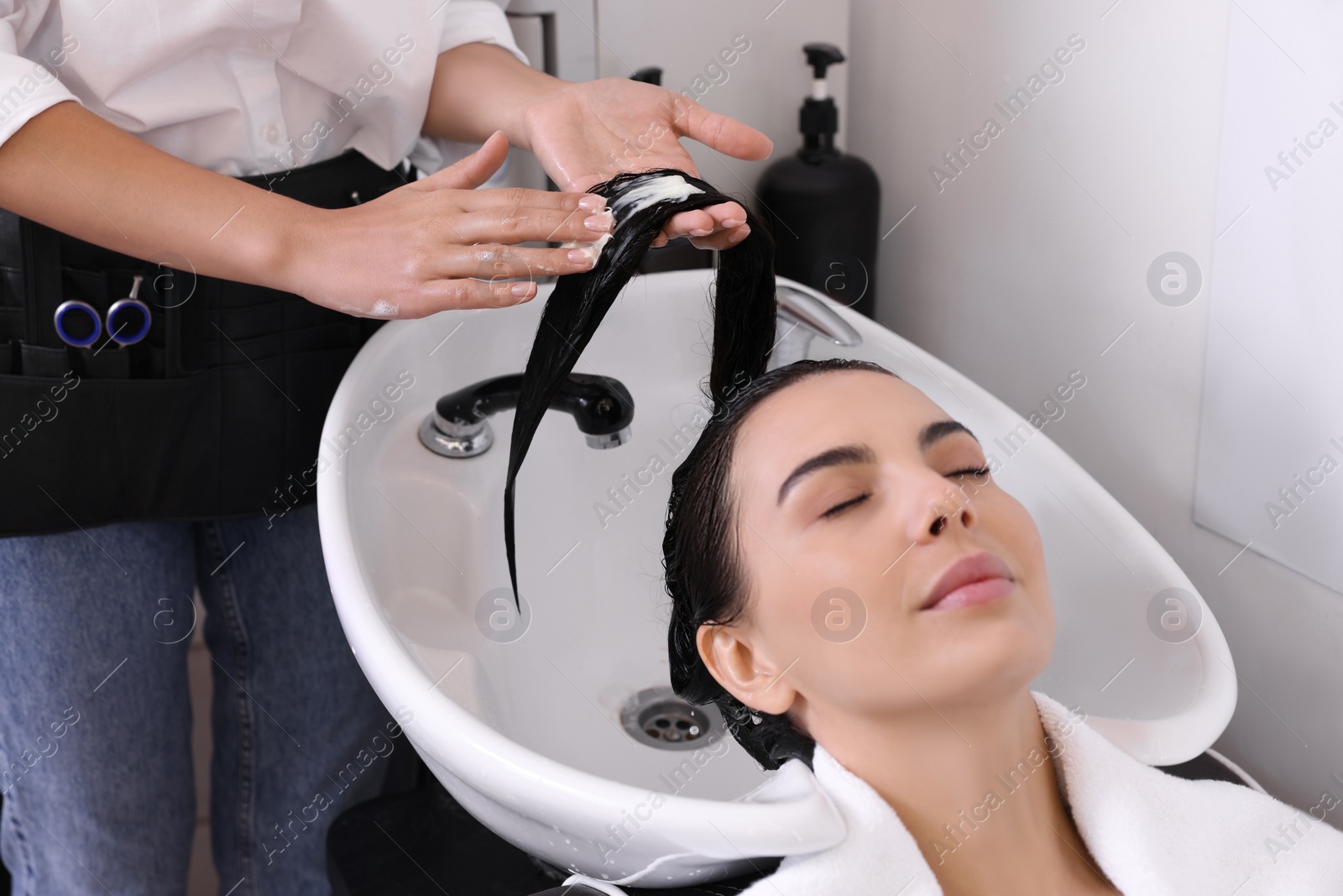 Photo of Professional hairdresser applying conditioner on woman's hair in beauty salon, closeup