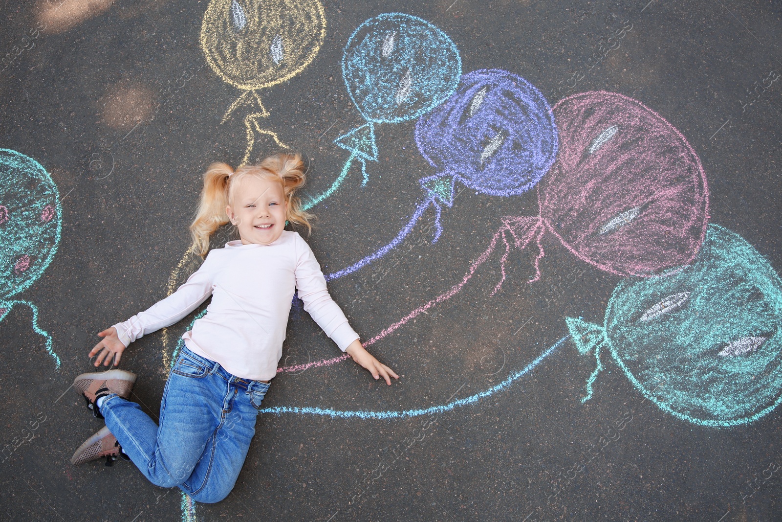 Photo of Little child lying near chalk drawing of balloons on asphalt, top view
