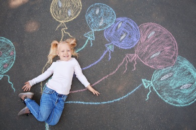 Photo of Little child lying near chalk drawing of balloons on asphalt, top view