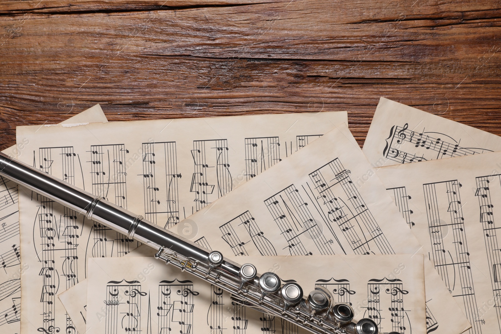 Photo of Sheets with musical notes and flute on wooden table, flat lay