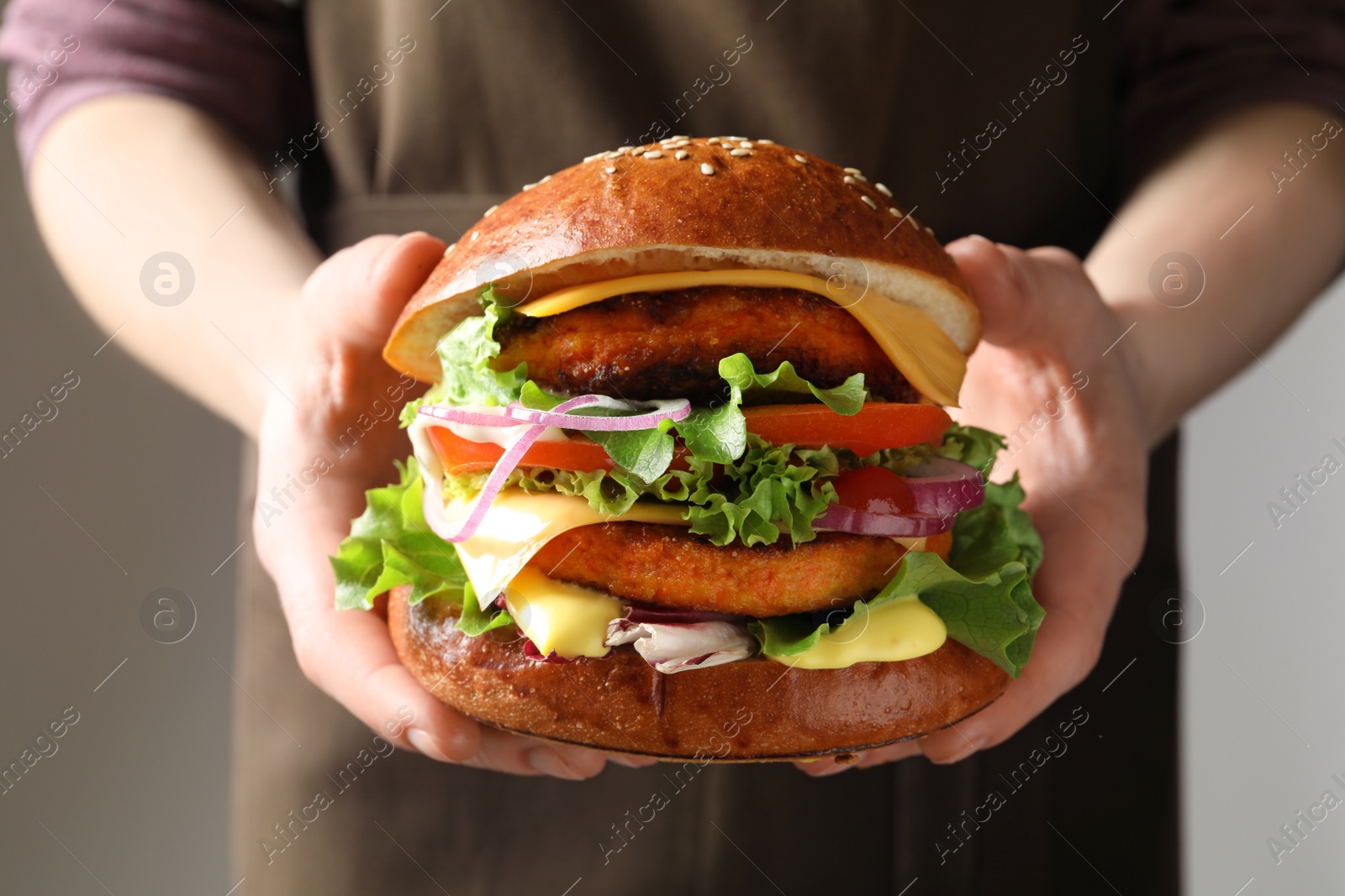 Photo of Woman holding tasty vegetarian burger on grey background, closeup