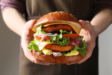 Photo of Woman holding tasty vegetarian burger on grey background, closeup