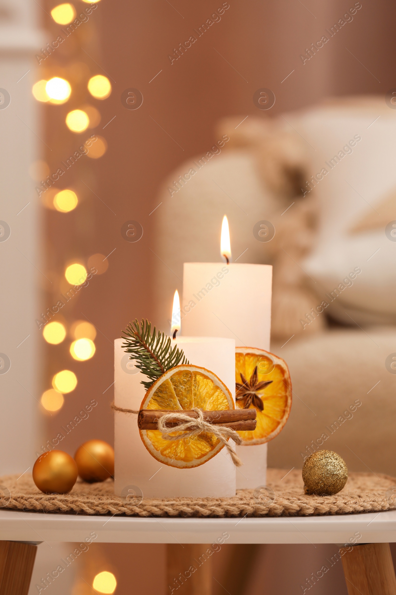 Photo of Beautiful burning candles decorated with dry orange slices and cinnamon sticks on white table indoors. Christmas atmosphere