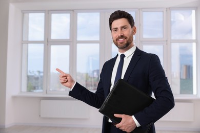 Photo of Happy real estate agent with leather portfolio pointing in new apartment