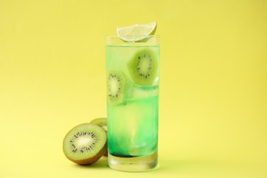 Glass of refreshing drink and cut kiwi on yellow background