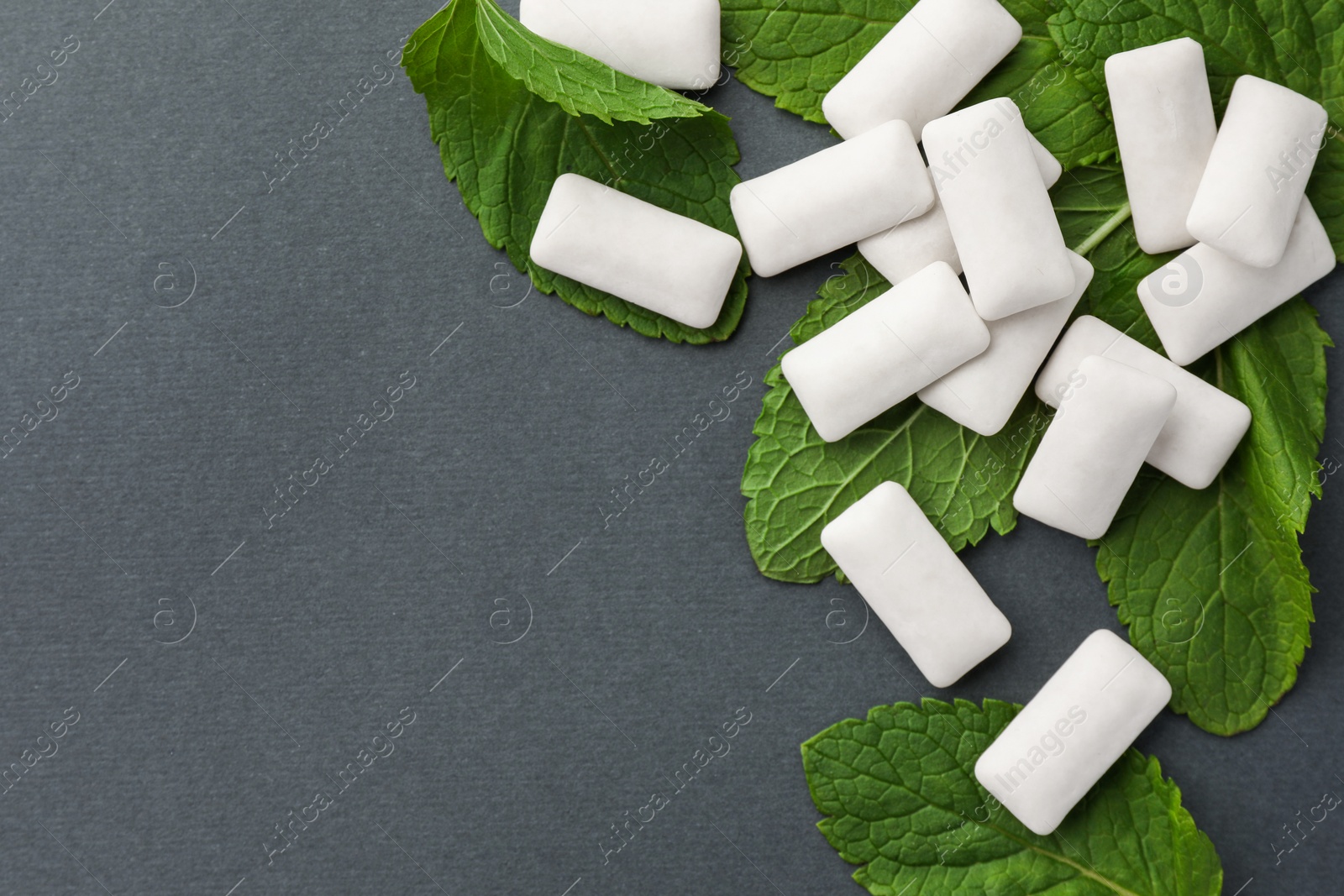 Photo of Tasty white chewing gums and mint leaves on grey background, flat lay. Space for text