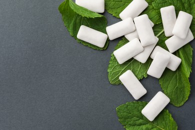 Photo of Tasty white chewing gums and mint leaves on grey background, flat lay. Space for text