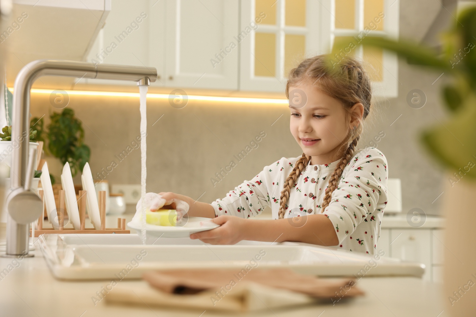 Photo of Little girl washing plate above sink in kitchen