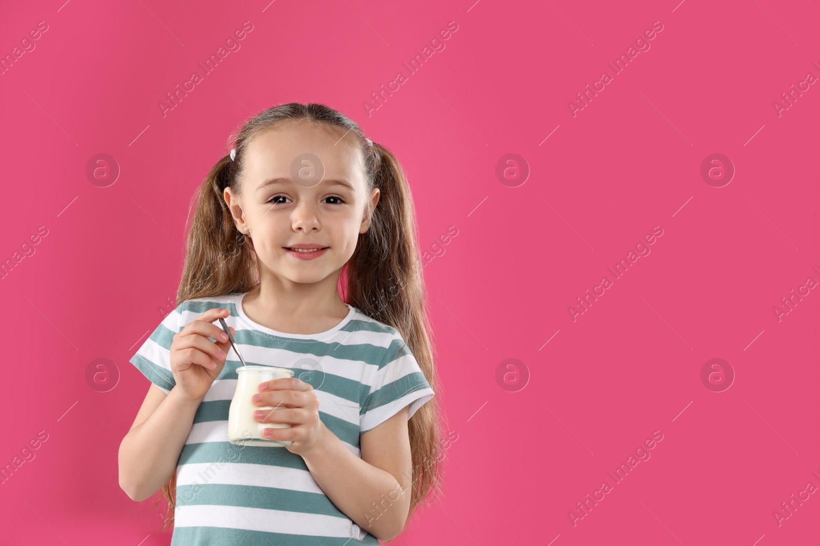 Photo of Cute little girl with tasty yogurt on pink background. Space for text