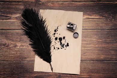 Feather pen, inkwell and vintage parchment with ink stains on wooden table, top view