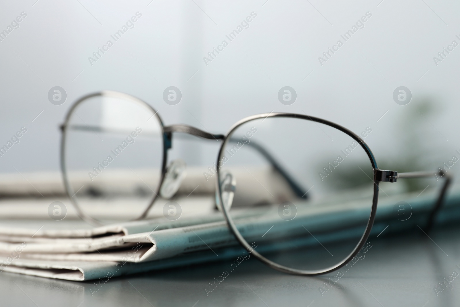 Photo of Stack of newspapers and glasses on grey table indoors, closeup