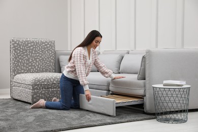 Woman making sleeping place for guest in living room. Convertible sofa