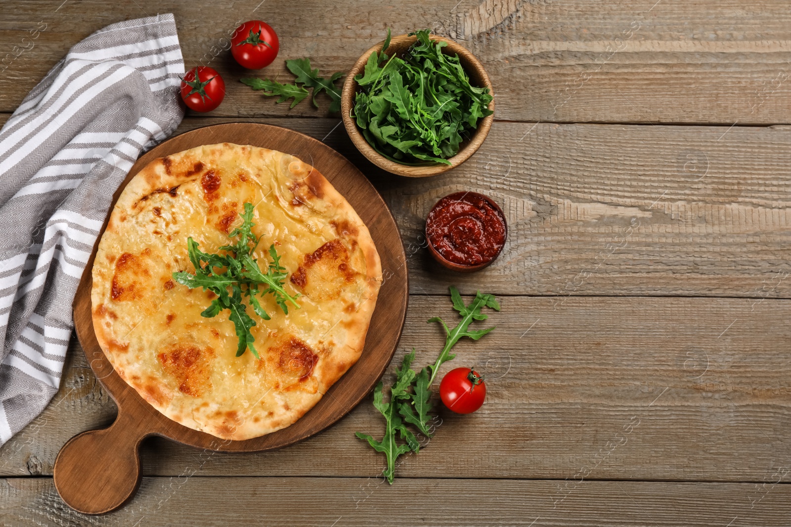 Photo of Delicious khachapuri with cheese, arugula, tomatoes and sauce on wooden table, flat lay. Space for text