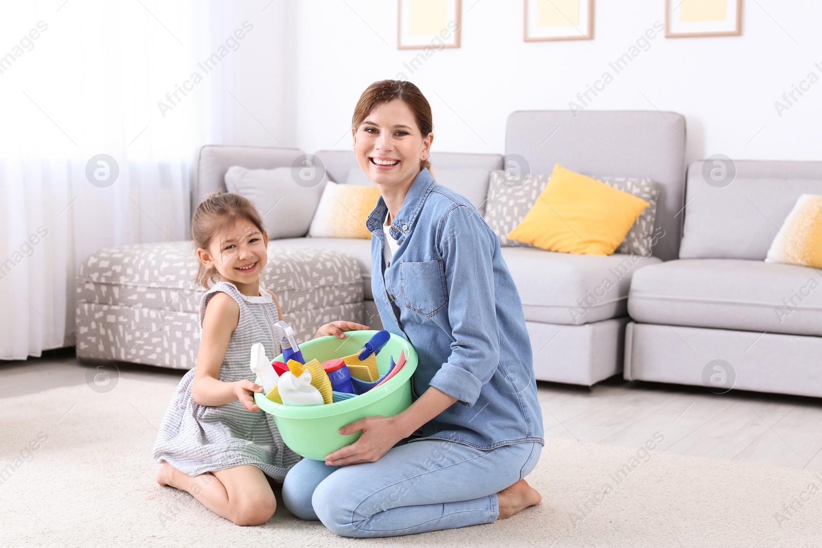 Photo of Housewife and daughter with basket full of detergents on carpet at home